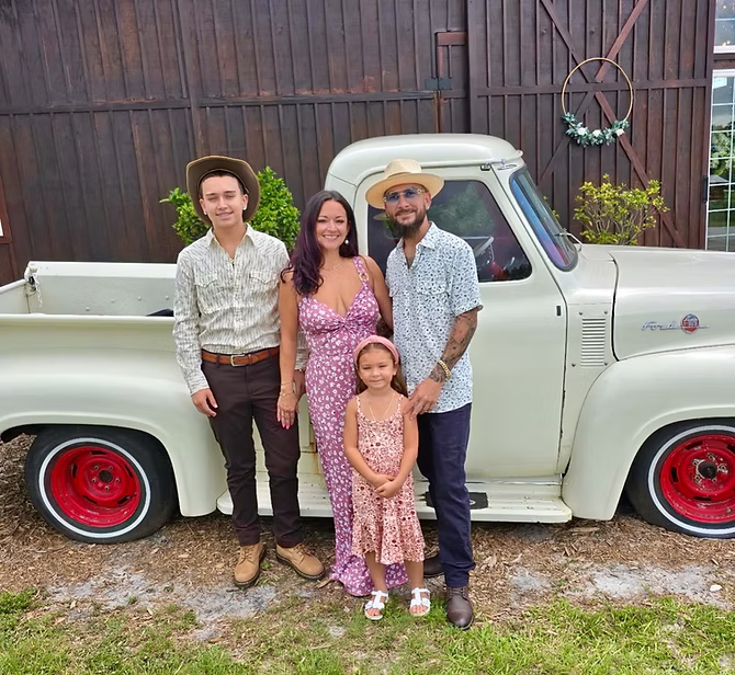 Brandon with his wife and two children beside a vintage truck